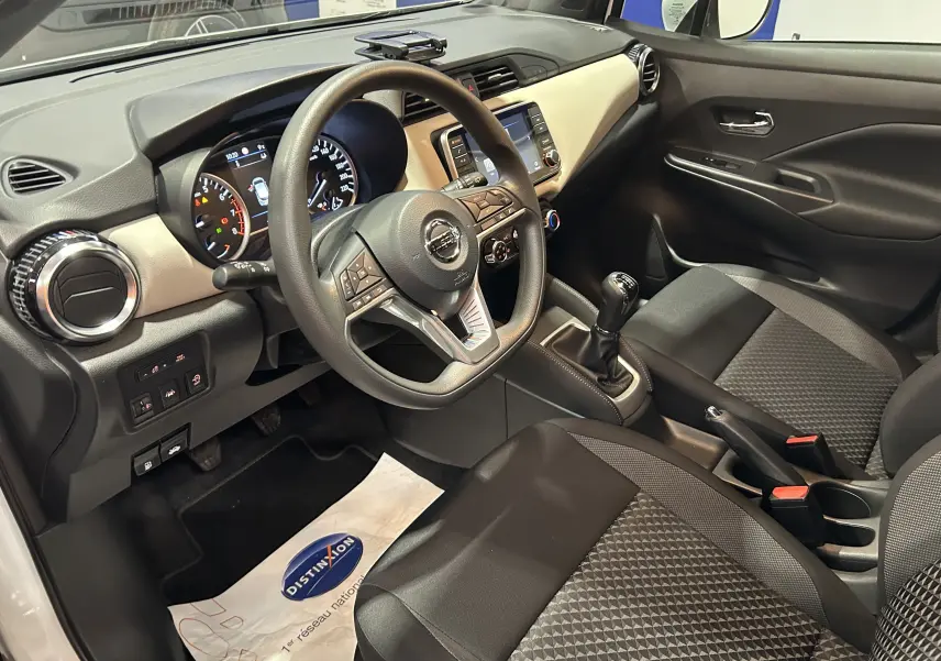 Vue intérieure côté conducteur de la Nissan Micra 2021, tableau de bord beige et noir avec volant multifonction et boîte manuelle.