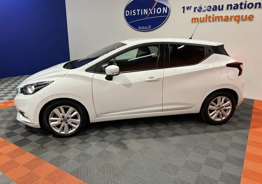 Profil côté gauche d'une Nissan Micra blanche 5 portes de 2021, en intérieur sur sol gris et orange avec logo Distinxion en arrière-plan.