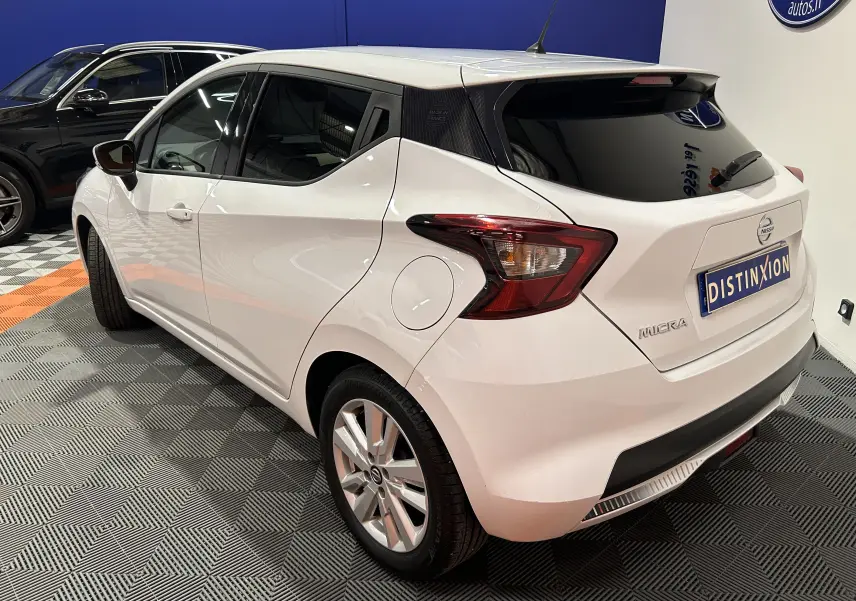 Vue 3/4 arrière droite d'une Nissan Micra blanche avec toit noir et vitres teintées dans un showroom.