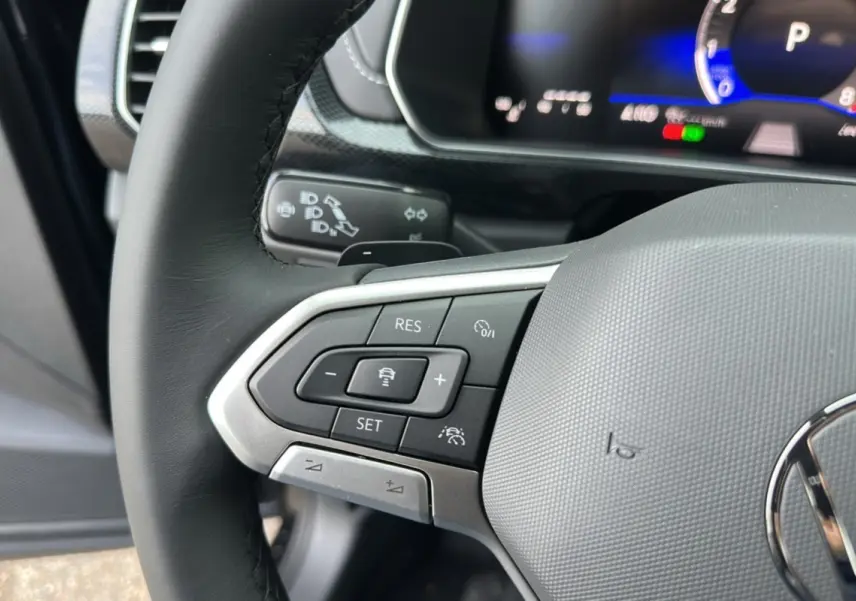 Gros plan sur le volant cuir multifonctions du Volkswagen T-Cross noir intense, avec commandes de régulateur adaptatif visibles.