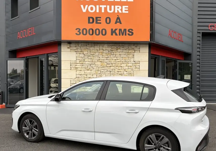 Vue latérale droite d'une Peugeot 308 blanche 2024 garée devant un bâtiment avec panneau orange "Votre nouvelle voiture".