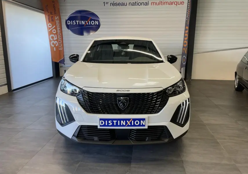 Vue avant d'un Peugeot 2008 blanc avec calandre noire et feux diurnes LED en griffes, en showroom intérieur.