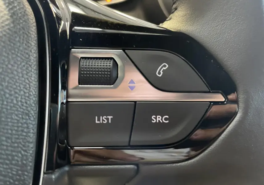 Gros plan sur les commandes multimédia noires du volant cuir du Peugeot 2008 blanc hybride, version 2026.