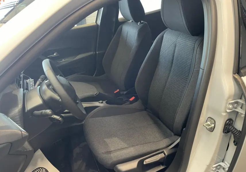 Vue intérieure côté conducteur de la Peugeot 2008 blanche, sièges tissu gris foncé avec surpiqûres contrastantes.