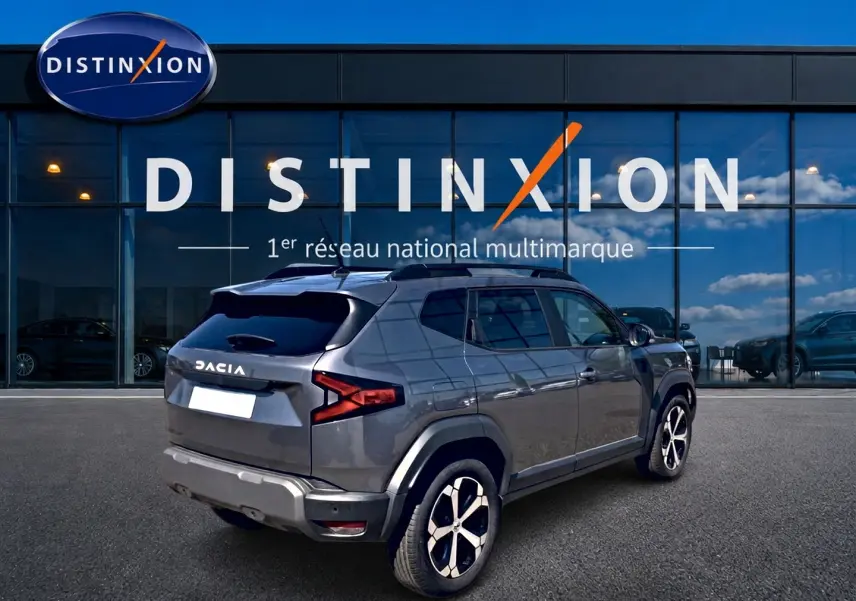 Vue 3/4 arrière droite du Dacia Duster gris schiste avec jantes alu, barres de toit et lunette arrière surteintée.