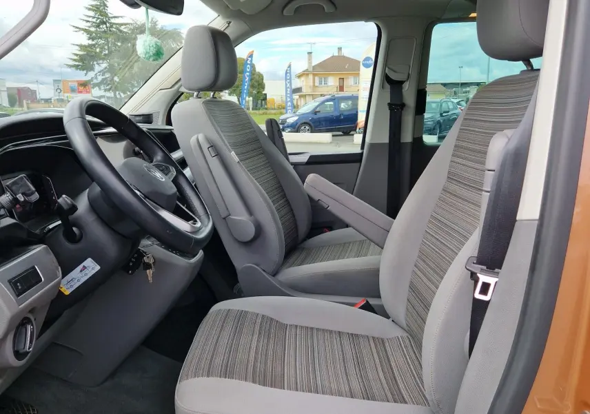 Vue intérieure côté conducteur du Volkswagen California Cooper bronze 2021, sièges gris à motifs rayés et toit relevable fermé.