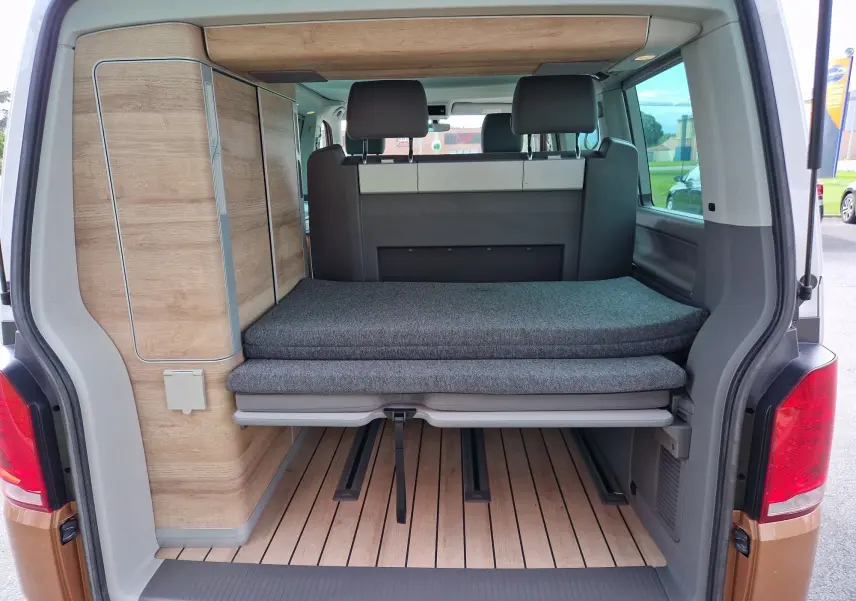 Vue arrière ouverte du Volkswagen California Cooper bronze 2021, montrant l'aménagement intérieur avec banquette et bois clair.