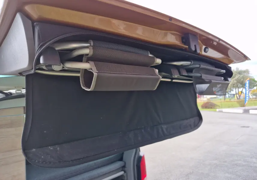 Détail du coffre arrière ouvert du Volkswagen California Cooper bronze 2021, montrant un store et des rangements intégrés.