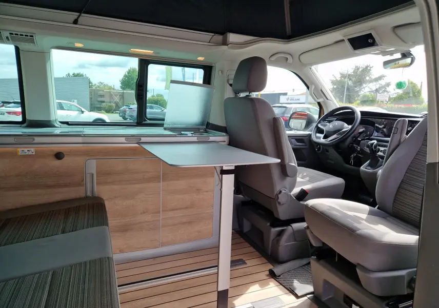 Intérieur du Volkswagen California Cooper bronze 2021 vu côté droit, avec table déployée et sièges gris aménagés.