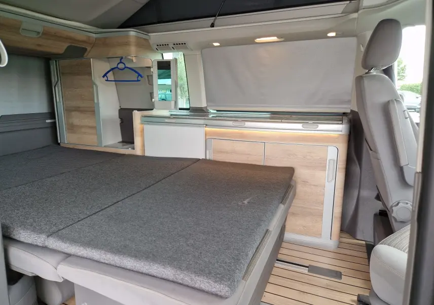 Intérieur du Volkswagen California 2.0 TDi 150 ch Coast 2021, vue latérale sur le coin nuit avec lit déplié et rangements bois clair.