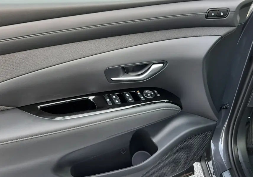 Intérieur côté gauche de la porte avant d'un Hyundai Tucson gris, avec commandes électriques et habillage noir.