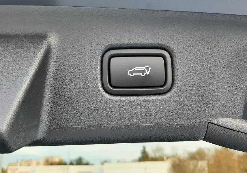 Bouton noir d'ouverture électrique du hayon sur le bord intérieur du coffre du Hyundai Tucson gris Ecotronic.