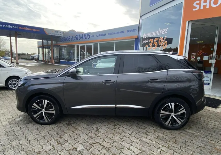 Profil côté gauche du Peugeot 3008 gris foncé GT 2023 garé devant un garage avec jantes alliage distinctives.