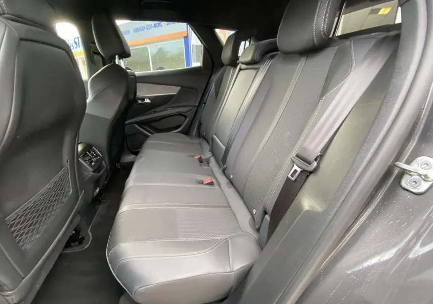 Vue côté droit des sièges arrière en cuir gris foncé du Peugeot 3008 2023, avec ceintures et filet de rangement au dos des sièges avant.