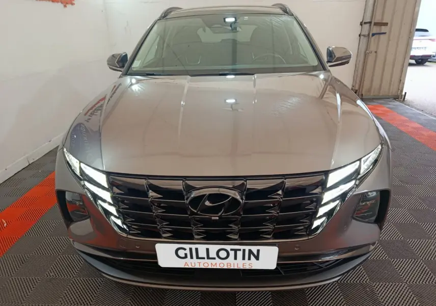 Vue avant d'un Hyundai Tucson marron 2022 avec calandre noire et phares LED allumés en intérieur showroom.