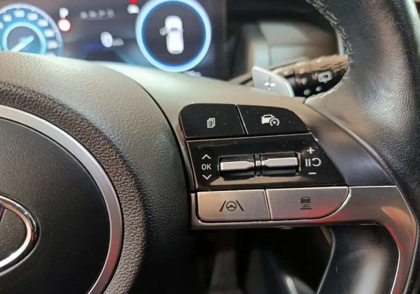 Gros plan sur les commandes à droite du volant cuir du Hyundai Tucson marron, avec affichage digital en arrière-plan.