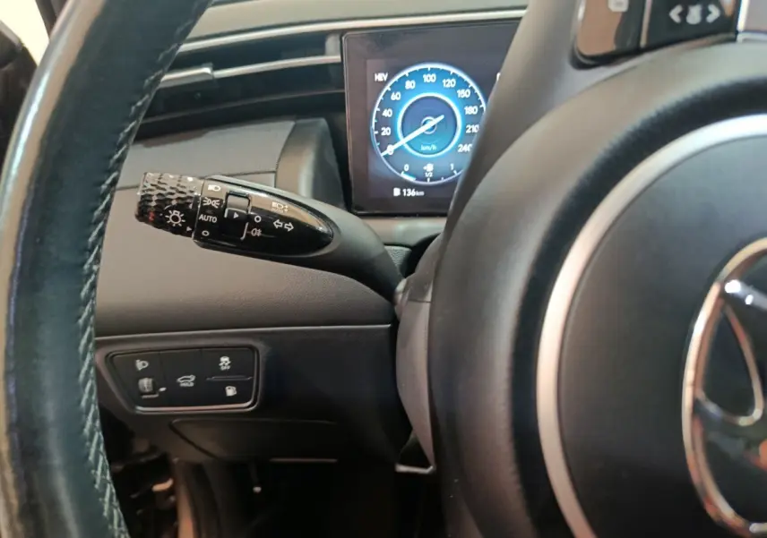 Gros plan sur le volant et la manette d'éclairage à gauche, avec tableau de bord numérique affichant la vitesse, intérieur noir.