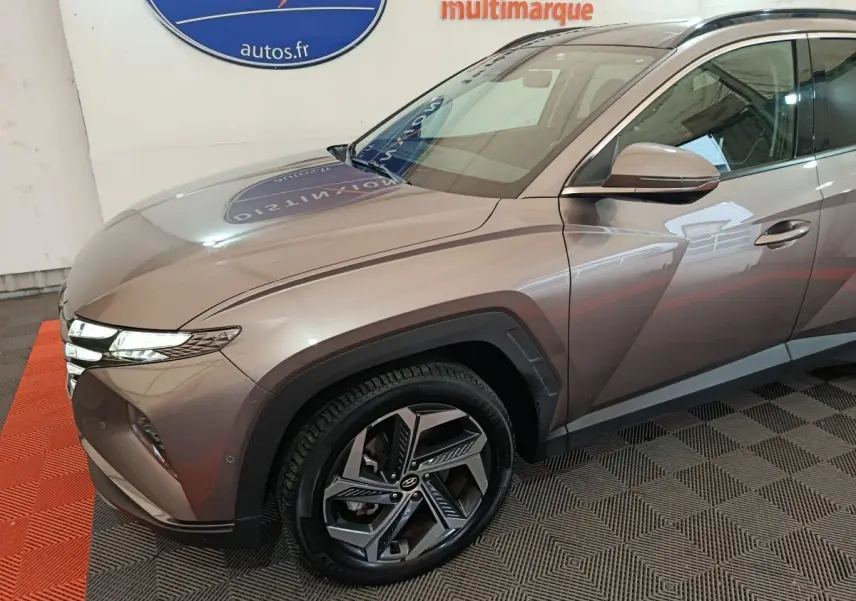 Vue 3/4 avant droit d'un Hyundai Tucson marron avec jantes alliage et feux LED distinctifs en intérieur showroom.