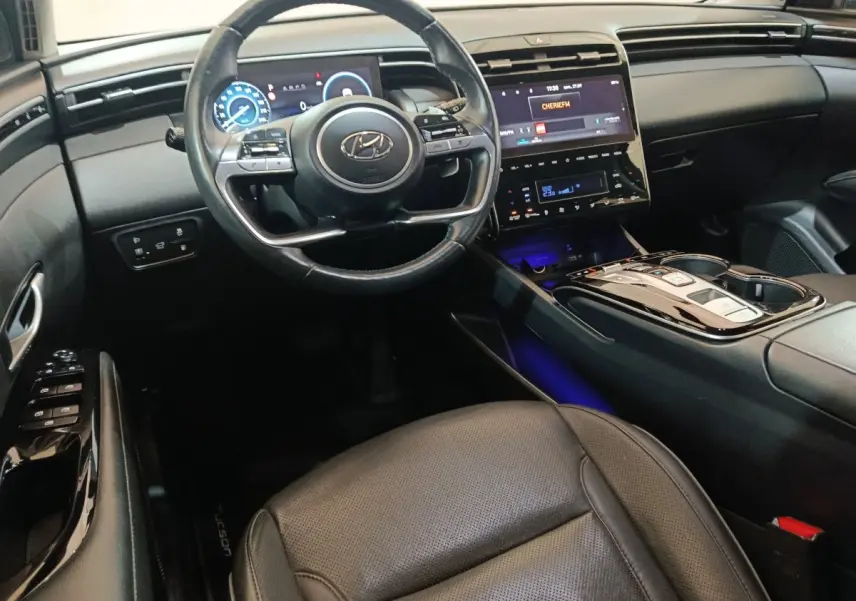 Intérieur noir du Hyundai Tucson 2022, vue côté conducteur sur volant cuir, tableau de bord digital et console centrale brillante.
