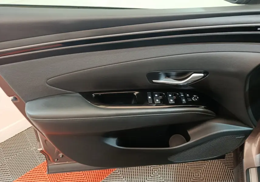 Vue rapprochée de la porte avant gauche marron du Hyundai Tucson 2022, avec commandes électriques et poignée argentée.