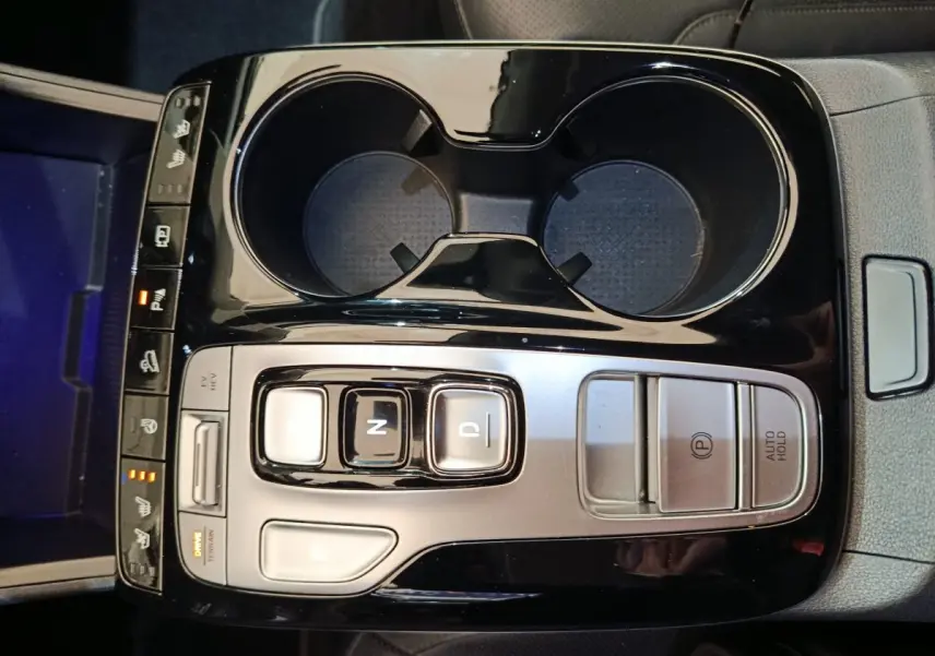 Vue plongeante sur la console centrale noire brillante du Hyundai Tucson marron 2022 avec commandes de boîte auto et porte-gobelets.