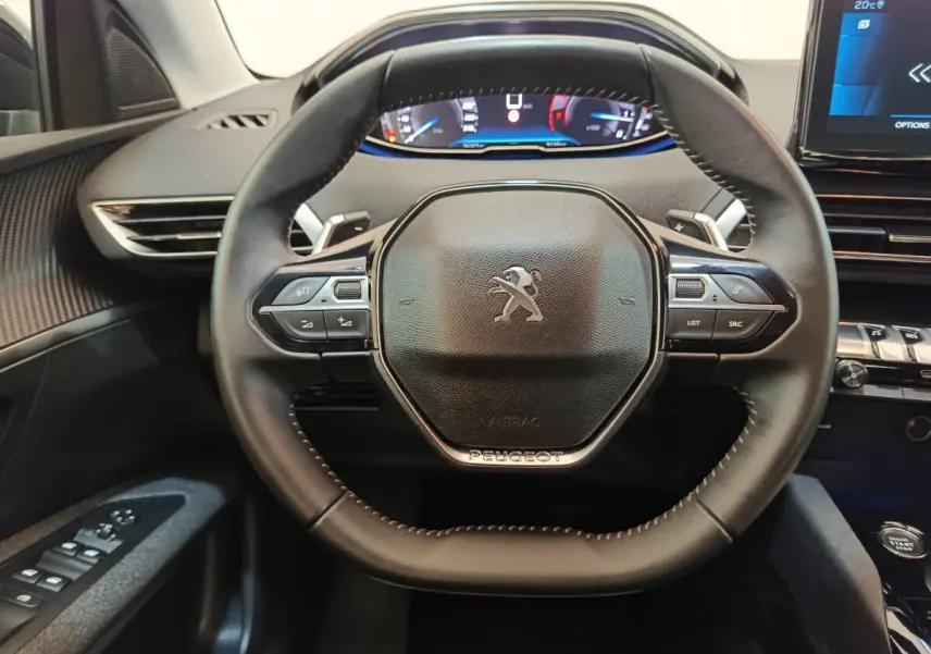 Vue rapprochée du volant cuir noir du Peugeot 3008 2022 avec commandes multifonctions et affichage digital en arrière-plan.
