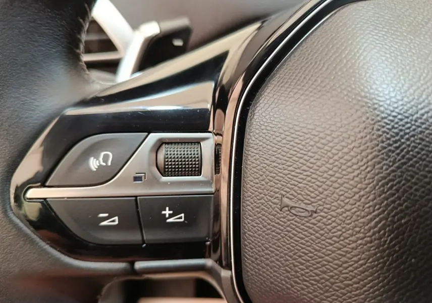 Gros plan sur les commandes de volume et de reconnaissance vocale sur le volant cuir noir du Peugeot 3008 gris foncé.