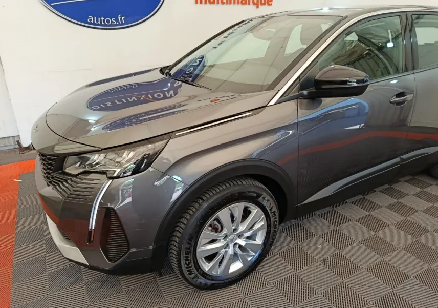 Vue 3/4 avant droit d'un Peugeot 3008 gris foncé avec phares LED et jantes alliage visibles en intérieur showroom.