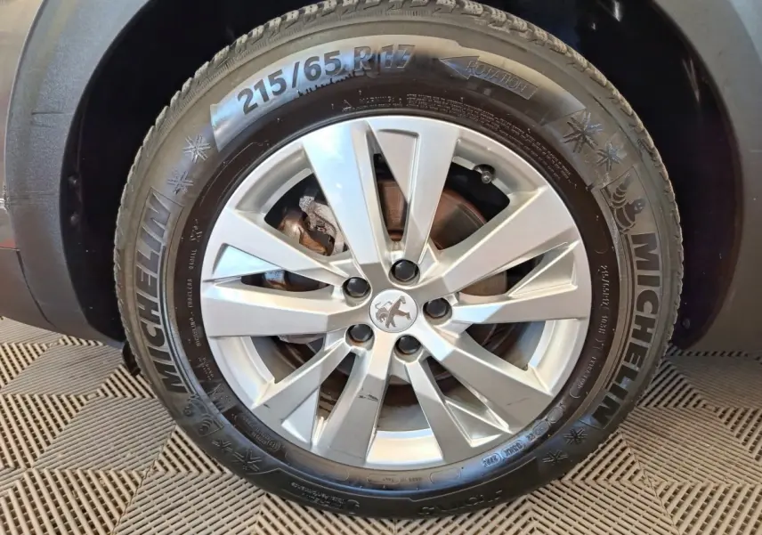 Gros plan sur la roue avant droite d’un Peugeot 3008 gris foncé avec jante alliage et pneu Michelin hiver.