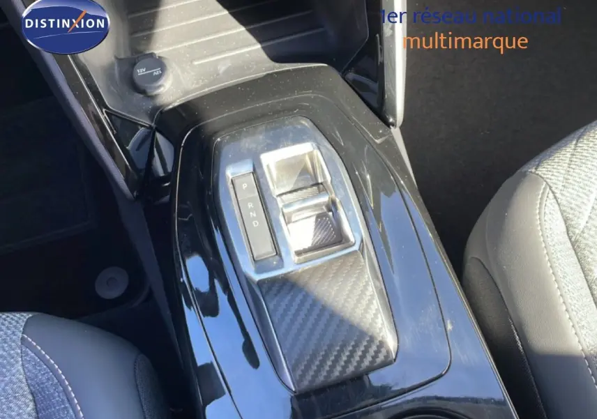 Gros plan sur la console centrale de la Peugeot 208 Hybrid 110ch, avec levier de boîte auto et finition carbone noire.