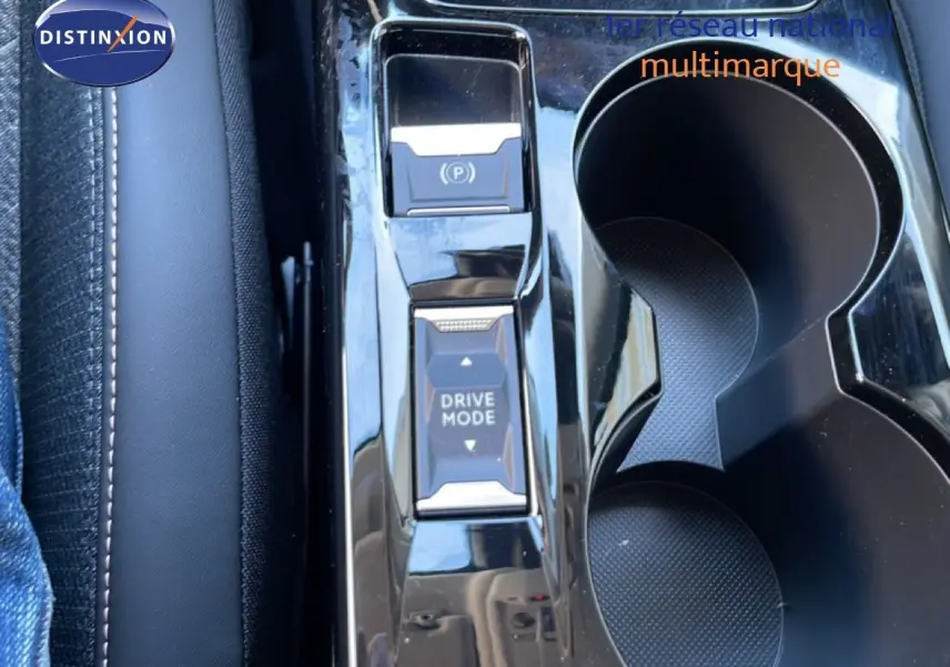 Gros plan sur la console centrale noire brillante de la Peugeot 208 Hybrid 110ch, avec boutons Drive Mode et frein à main électrique.