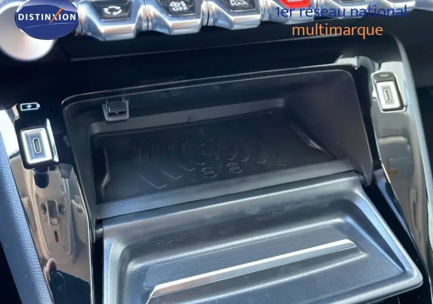 Gros plan sur la console centrale noire du Peugeot 208 Hybrid 110ch, montrant le compartiment de recharge sans fil et ports USB.