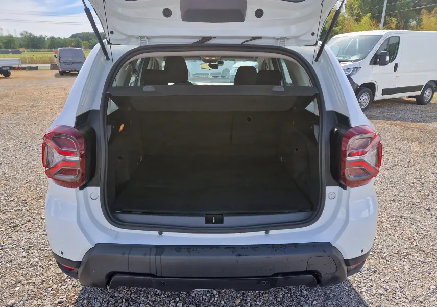 Vue arrière d'un Dacia Duster blanc 2023 avec coffre ouvert montrant un espace de chargement vide et un hayon relevé.