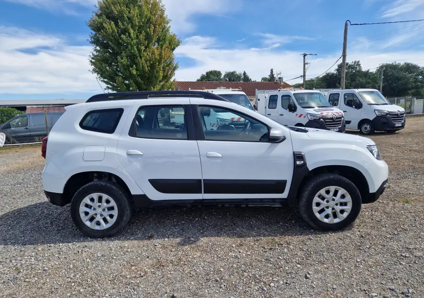 Vue de profil côté gauche d'un Dacia Duster blanc 4x4 2023 avec protections noires et jantes alliage 16 pouces.