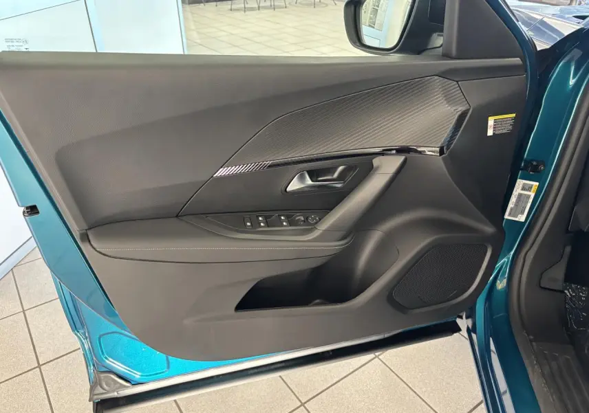 Vue intérieure de la porte avant gauche bleu métallisé du Peugeot 2008 avec insert carbone et haut-parleur intégré.