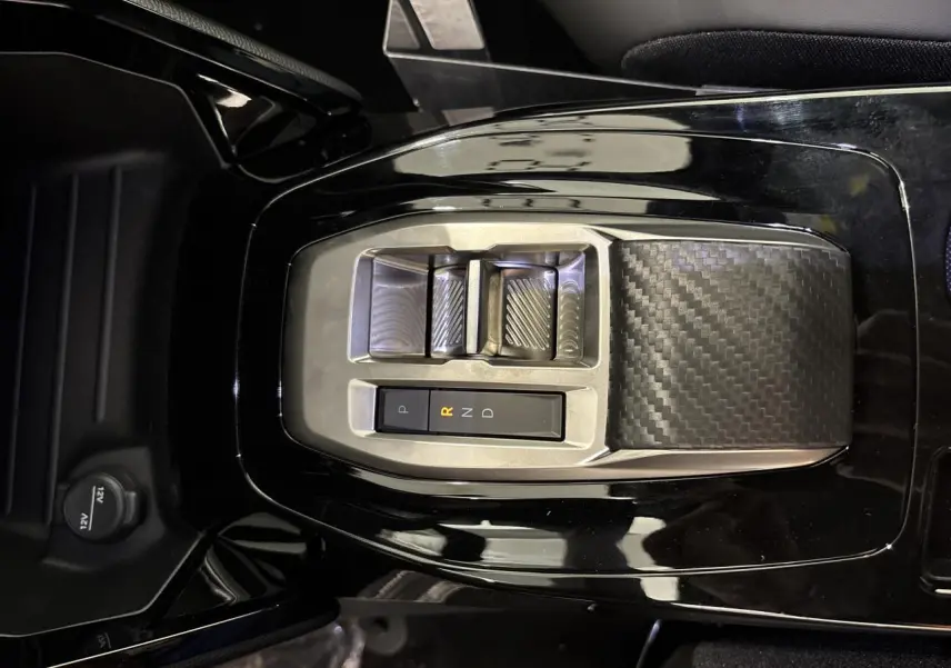 Vue plongeante sur la console centrale noire brillante du Peugeot 2008 hybride avec sélecteur de boîte automatique en carbone.