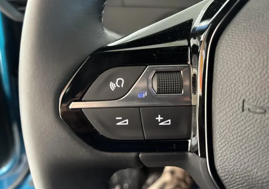 Gros plan sur les commandes noires du volant cuir du Peugeot 2008 bleu, avec bouton volume et assistant vocal.