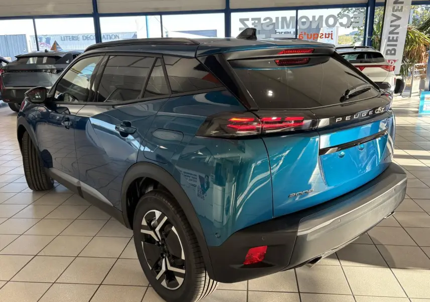 Peugeot 2008 bleu 3/4 arrière droit en showroom, feux LED et jantes alliage bi-ton visibles.