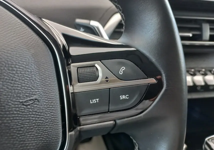 Gros plan sur les commandes gauche du volant cuir noir du Peugeot 5008 gris foncé, avec boutons LIST et SRC visibles.
