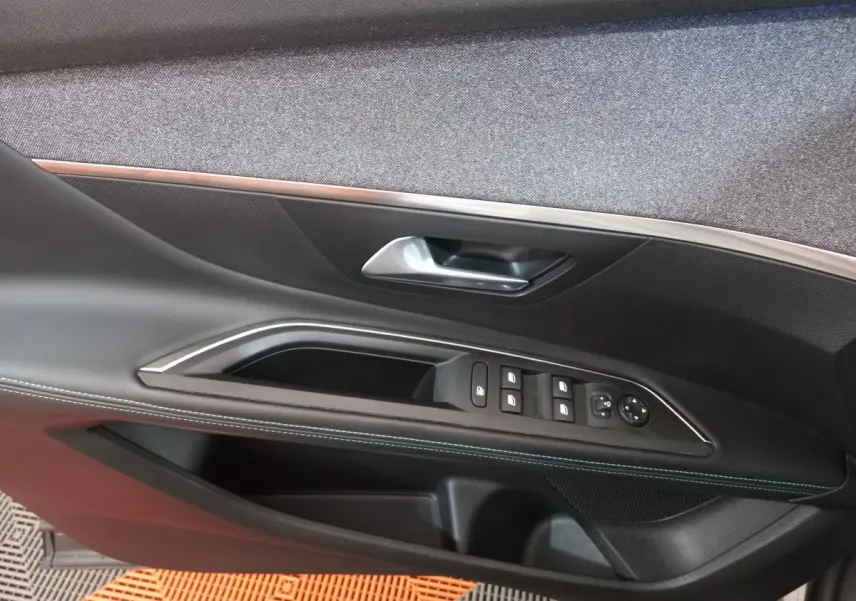 Gros plan sur la porte côté conducteur du Peugeot 5008 gris foncé, montrant les commandes des vitres et la poignée intérieure.
