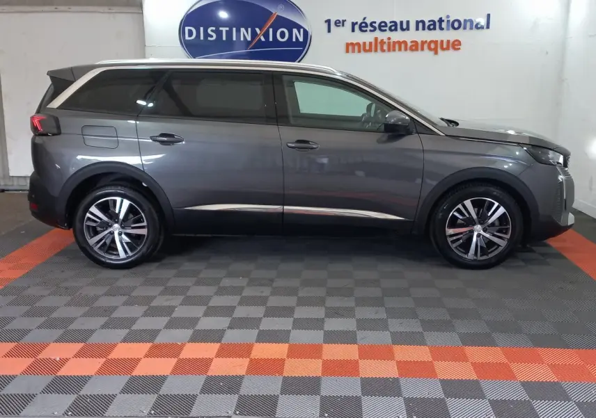 Profil droit d'un Peugeot 5008 gris foncé 2021 dans un showroom avec logo Distinxion en arrière-plan.
