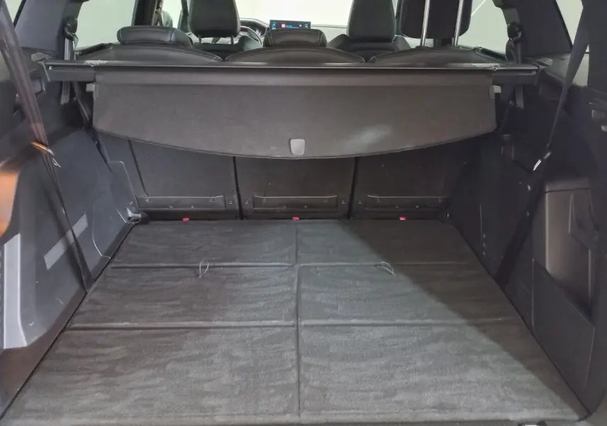 Coffre spacieux du Peugeot 5008 gris foncé vu de l'arrière avec banquette rabattue et cache-bagages déployé.