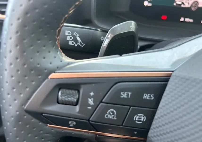 Gros plan sur les commandes au volant perforé du CUPRA Formentor blanc neige, avec palettes de changement de rapports visibles.