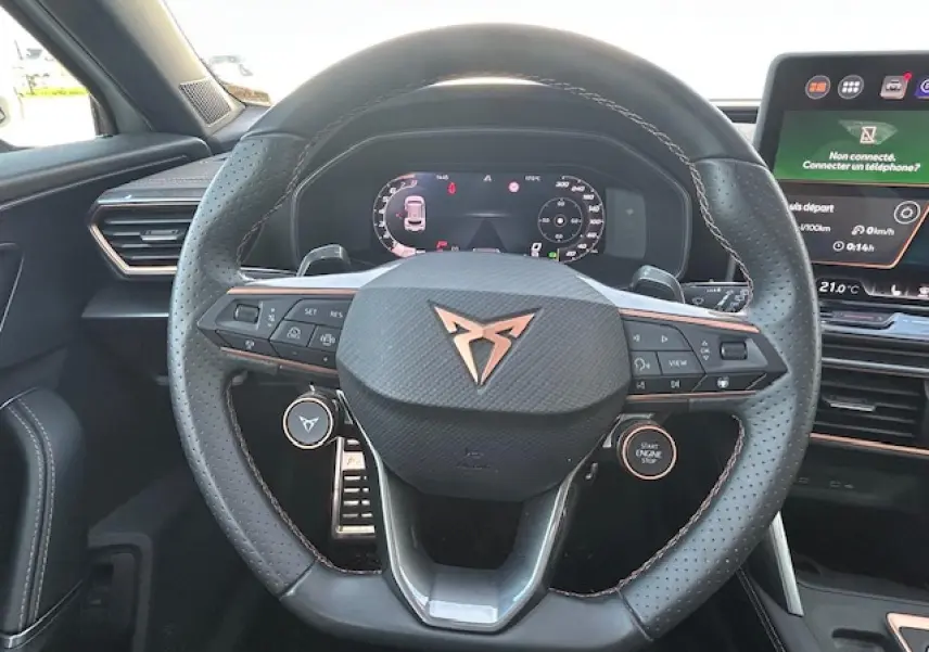 Vue rapprochée du volant cuir perforé avec logo CUPRA cuivré et tableau de bord digital du Formentor blanc neige 2025.