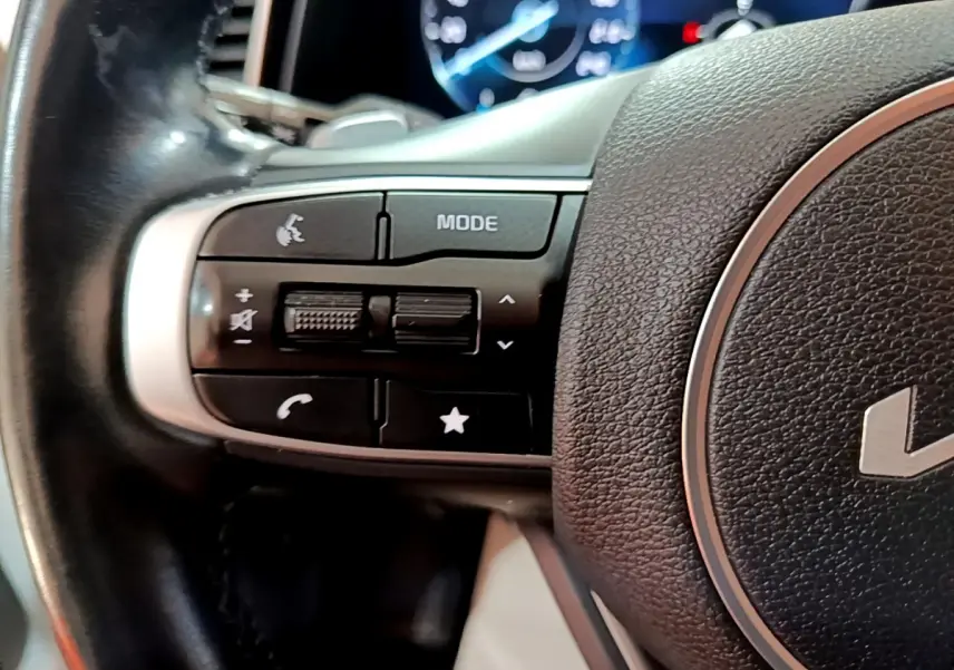 Gros plan sur les commandes gauche du volant cuir noir du KIA SPORTAGE blanc 2022 avec affichage numérique en arrière-plan.