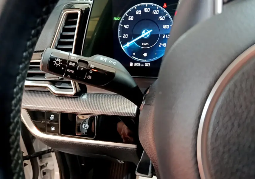 Vue intérieure rapprochée du tableau de bord et volant du KIA SPORTAGE blanc, affichage digital du compteur et commandes lumineuses.