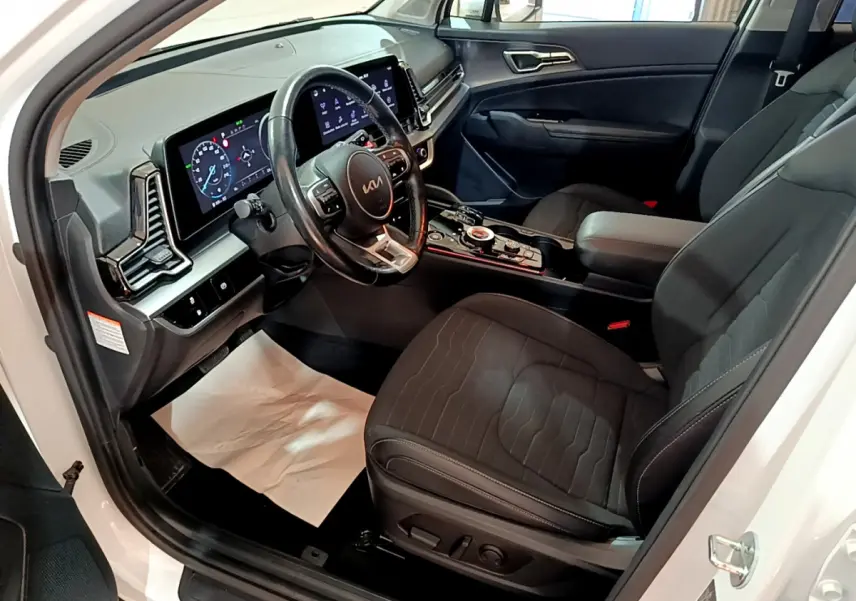 Intérieur avant du Kia Sportage blanc 2022, vue côté conducteur, avec tableau de bord digital et sièges noirs.