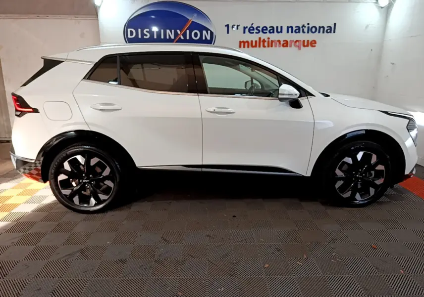 Profil droit d'un KIA SPORTAGE blanc 2022 avec jantes noires et détails noirs contrastants sous un éclairage intérieur.