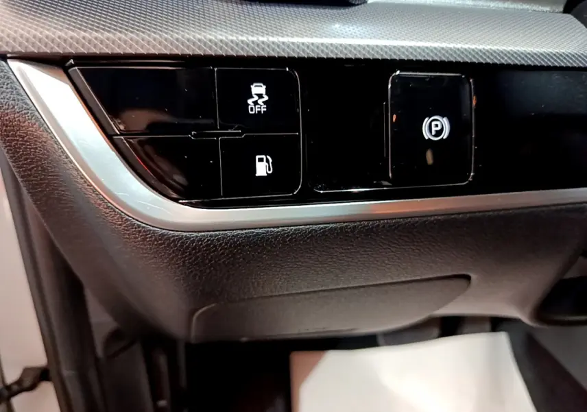 Gros plan sur les commandes noires du tableau de bord du Kia Sportage blanc 2022, avec boutons d'assistance et frein à main électrique.