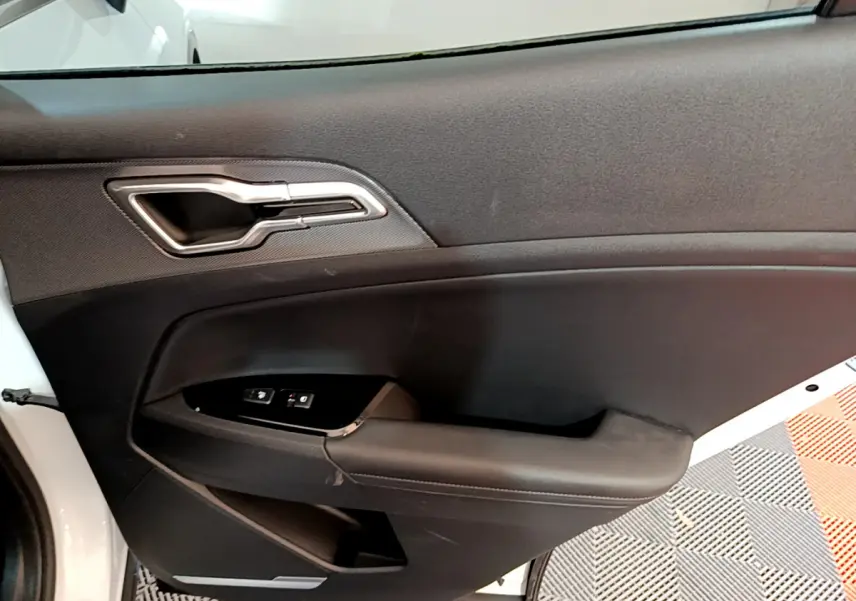 Vue intérieure de la porte avant gauche du KIA SPORTAGE blanc, avec poignée argentée et commandes de vitres.